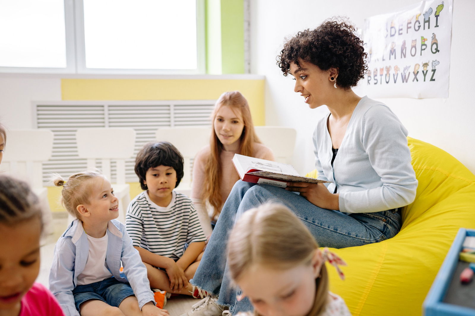 woman sitting on yellow beanbag reading to children